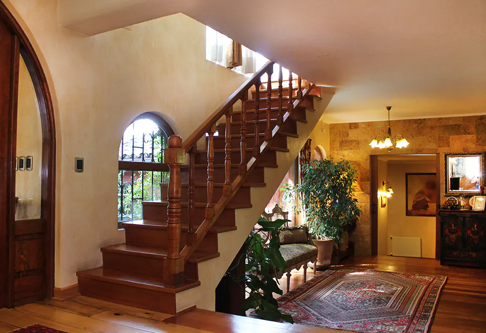 Interior view of a home featuring a wooden staircase, arched window, and patterned rug on a hardwood floor.
