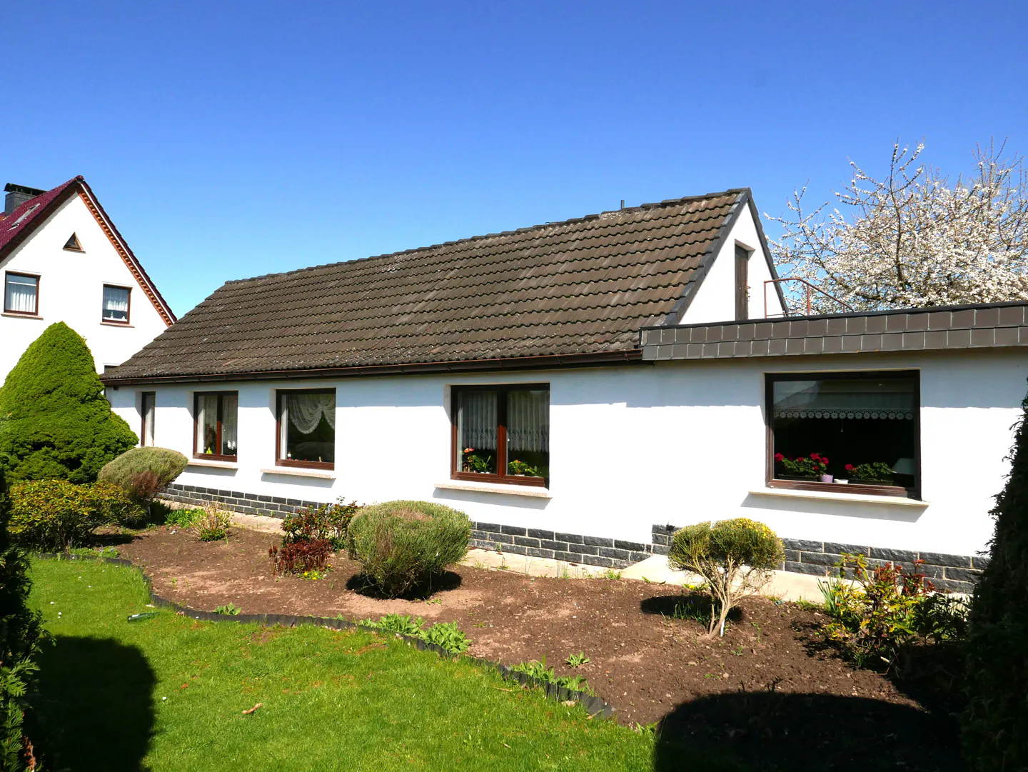 A white, one-story house with a brown tiled roof and a well-manicured lawn under a clear blue sky.