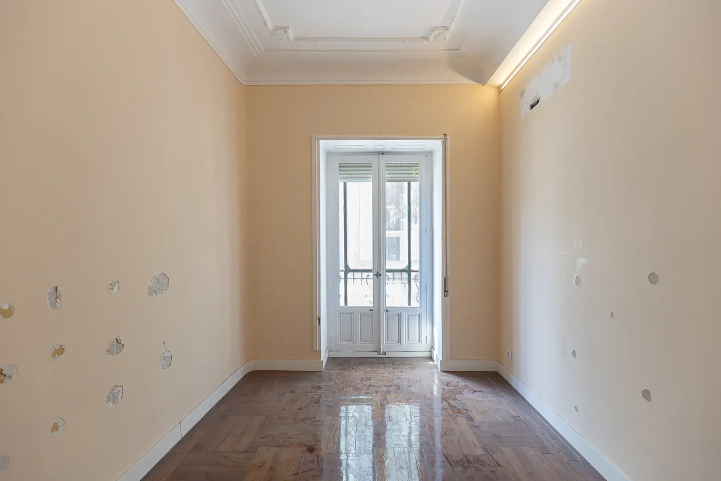 Empty room with peach-colored walls, worn wooden floors, and white French doors leading to a balcony.