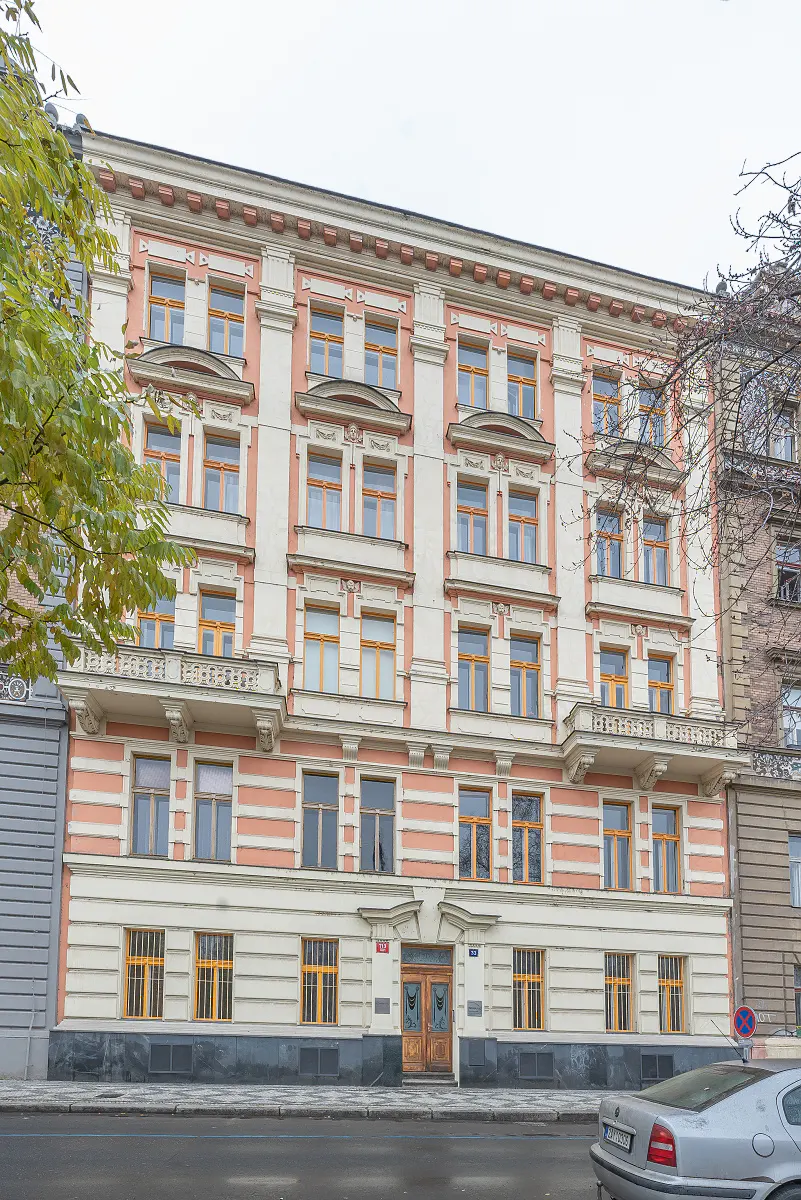 Exterior of a four-story building with peach and white facade, yellow window frames, and a gray car parked in front.