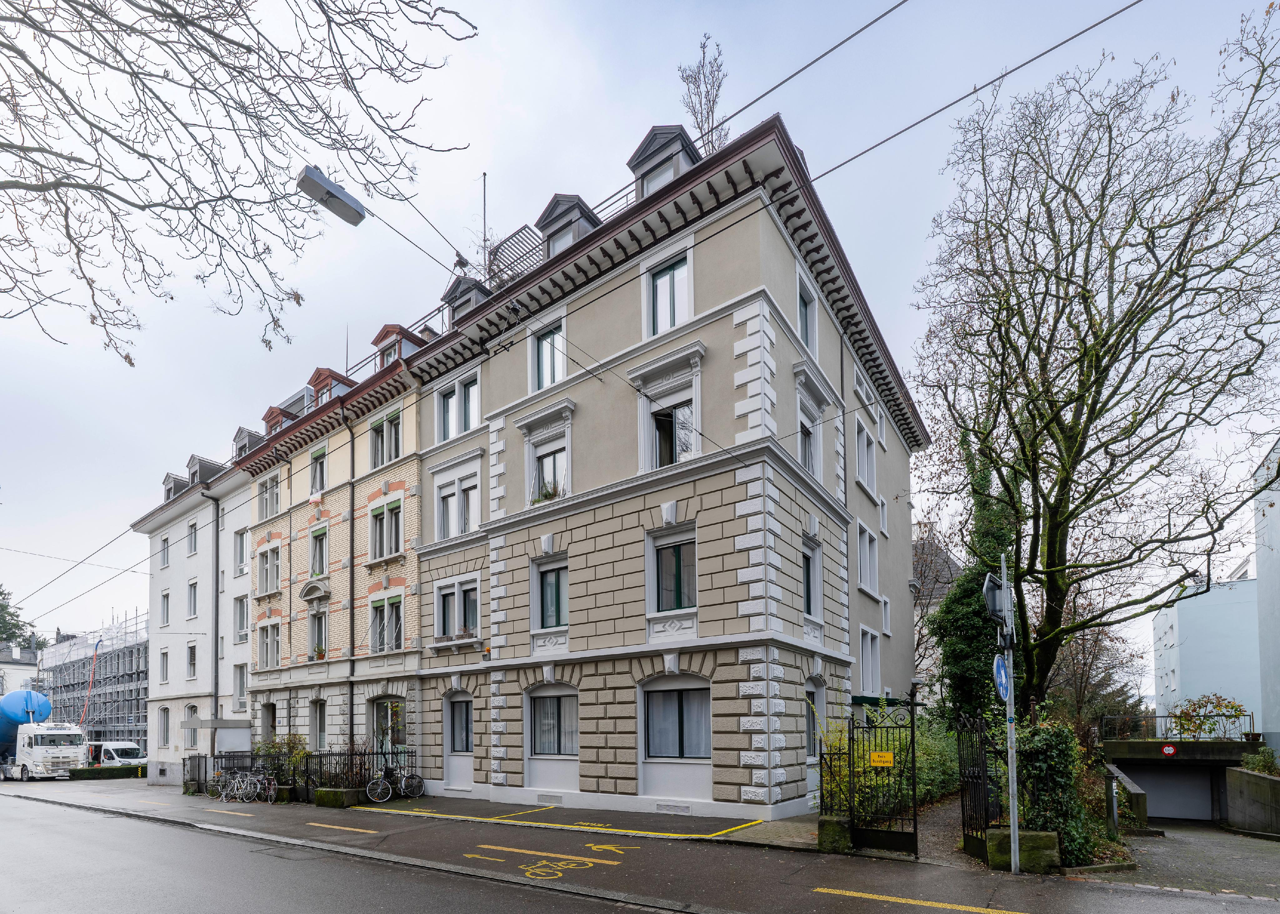 A multi-story corner apartment building with a beige facade, stone-block detailing, and dormer windows on a city street.