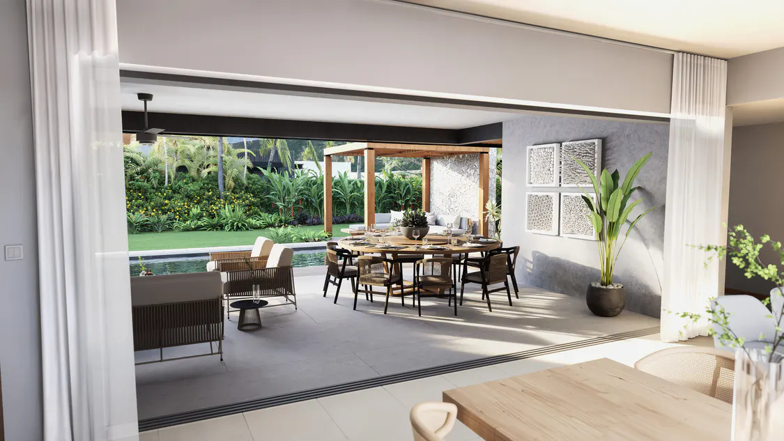 Open-concept living area with a round dining table, outdoor seating, and lush green landscaping.