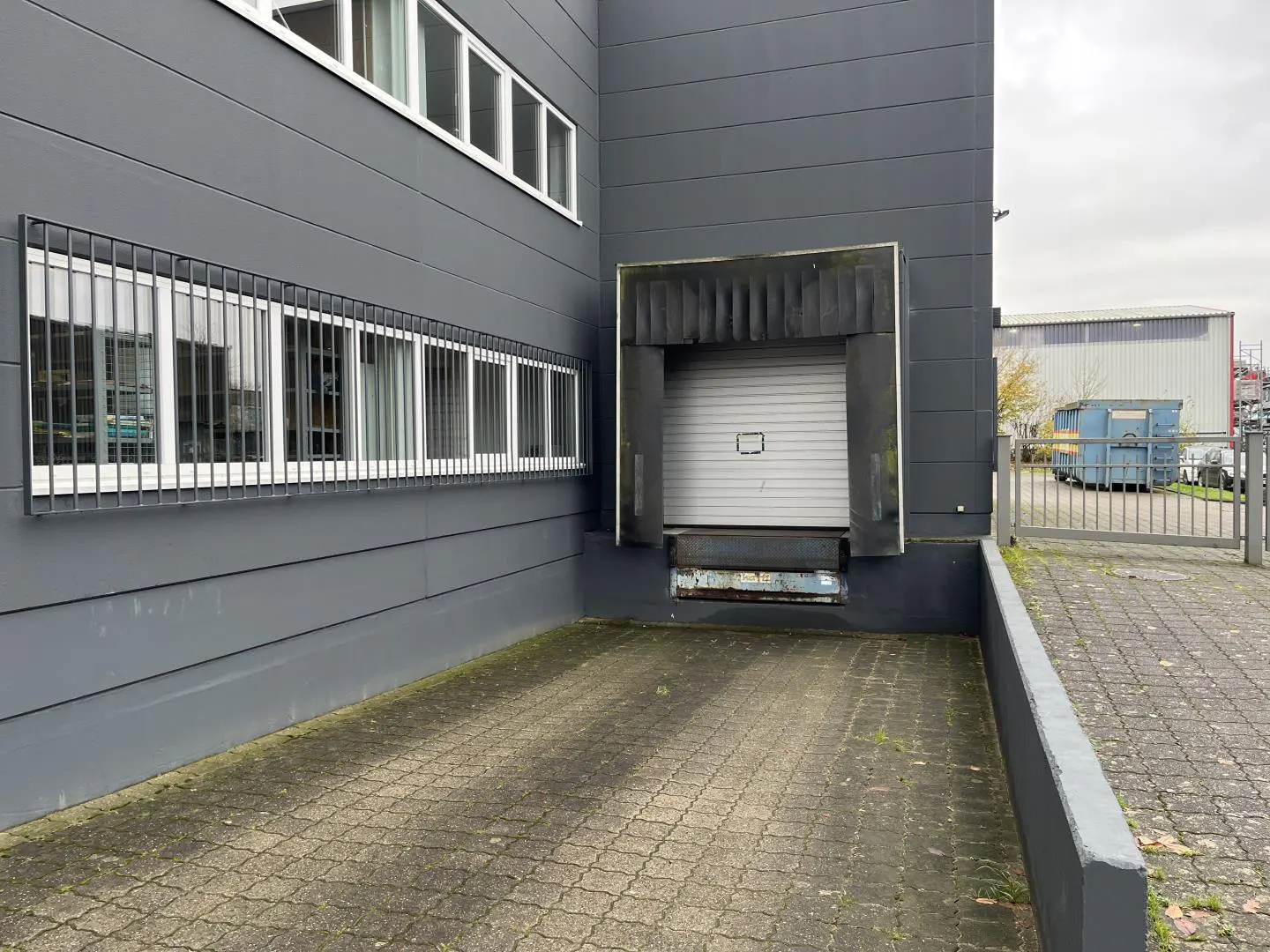 Exterior of a gray industrial building with a loading dock and barred windows.