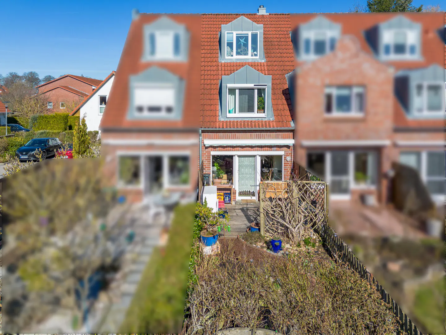 Exterior view of a red brick townhouse with a red tile roof and a small garden in front.