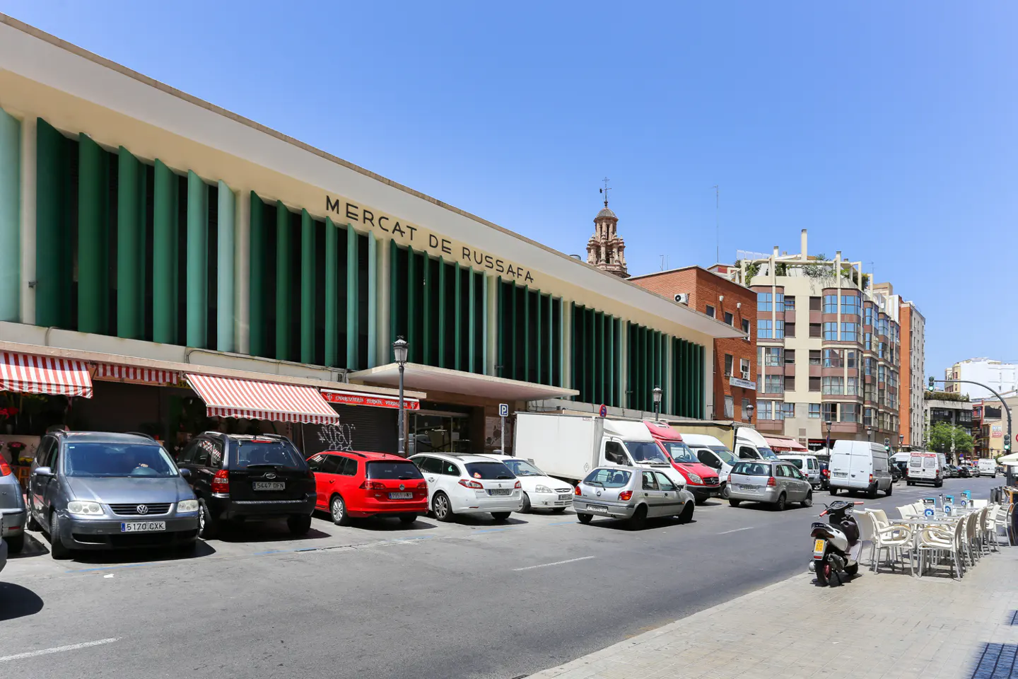 Exterior view of the Mercat de Russafa in Valencia, Spain, with parked cars and sidewalk cafe seating.