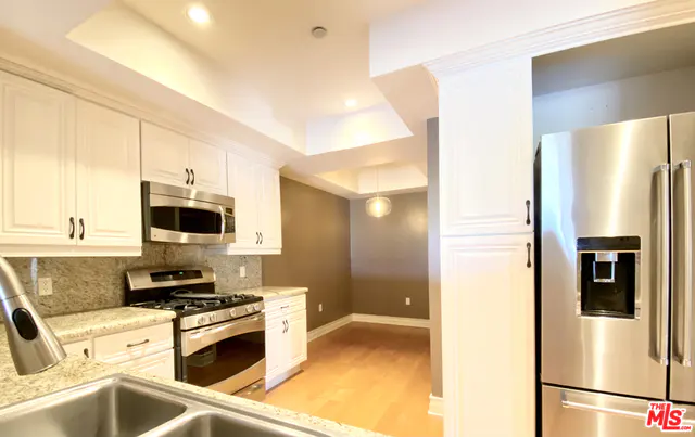 A kitchen with white cabinets, stainless steel appliances, and a dining area with wood floors.