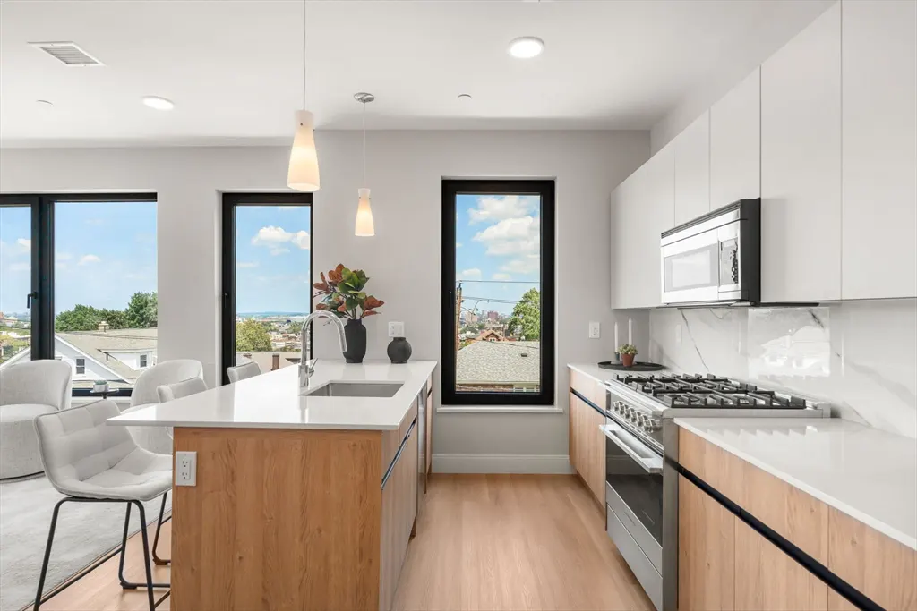 Bright, modern kitchen with white cabinets, wood island, and stainless steel appliances. Large windows offer a city view.