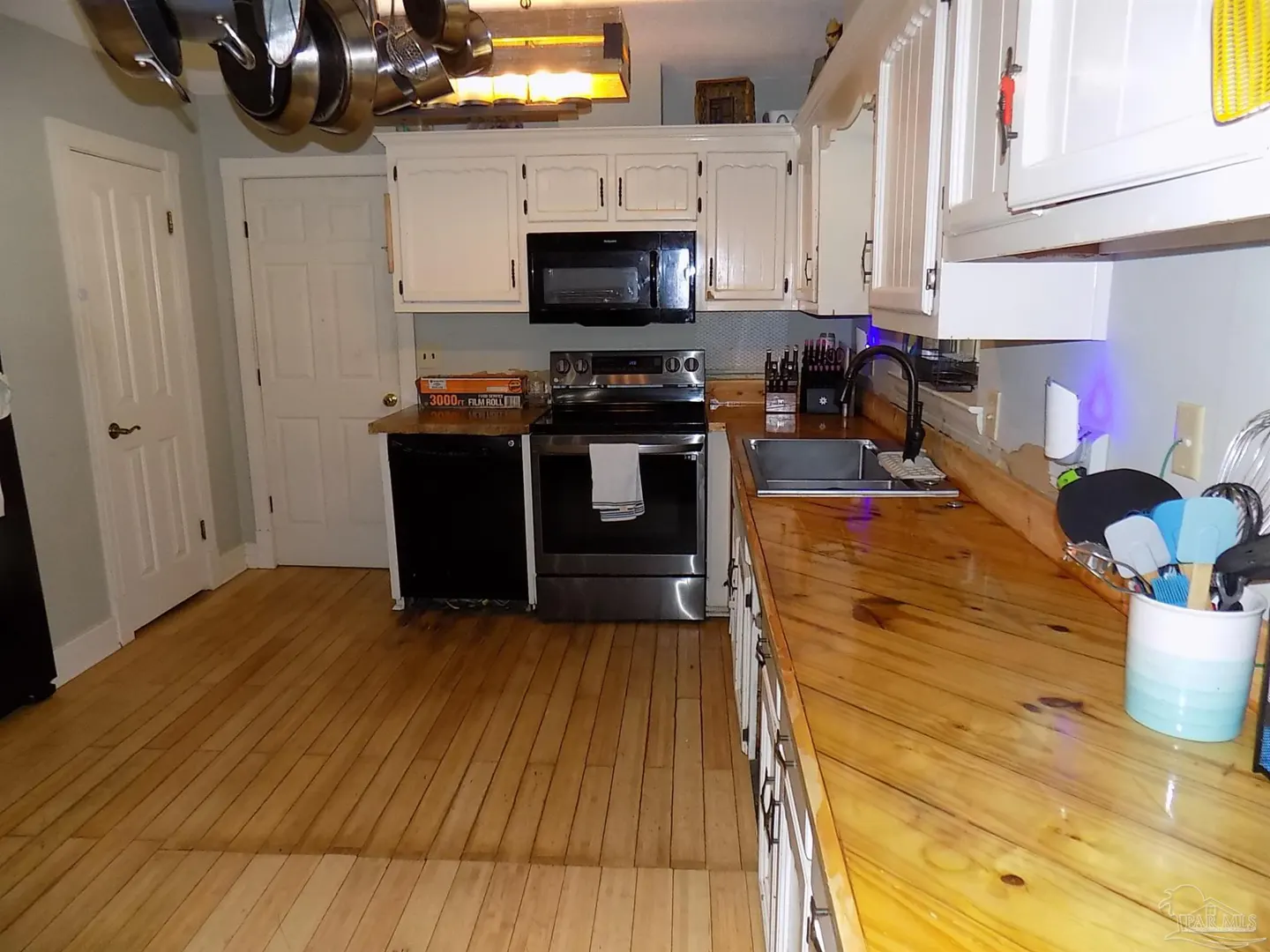 A kitchen with wood floors, white cabinets, stainless steel appliances, and wood countertops.