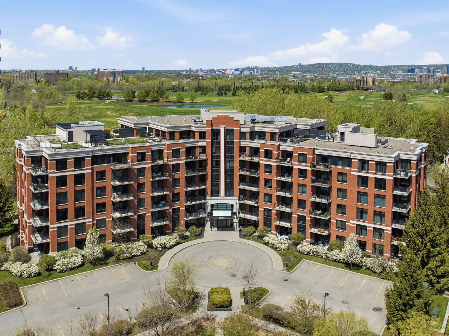 Aerial view of a red brick apartment building with balconies, a circular driveway, and green trees.