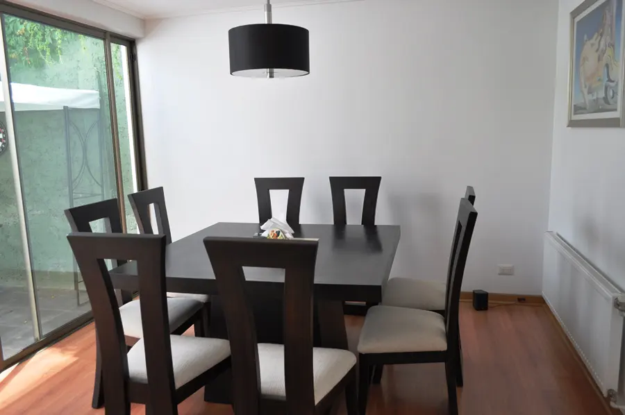 Dining room with a dark wood table, six chairs, and a black drum pendant light. A sliding glass door leads to a green outdoor space.