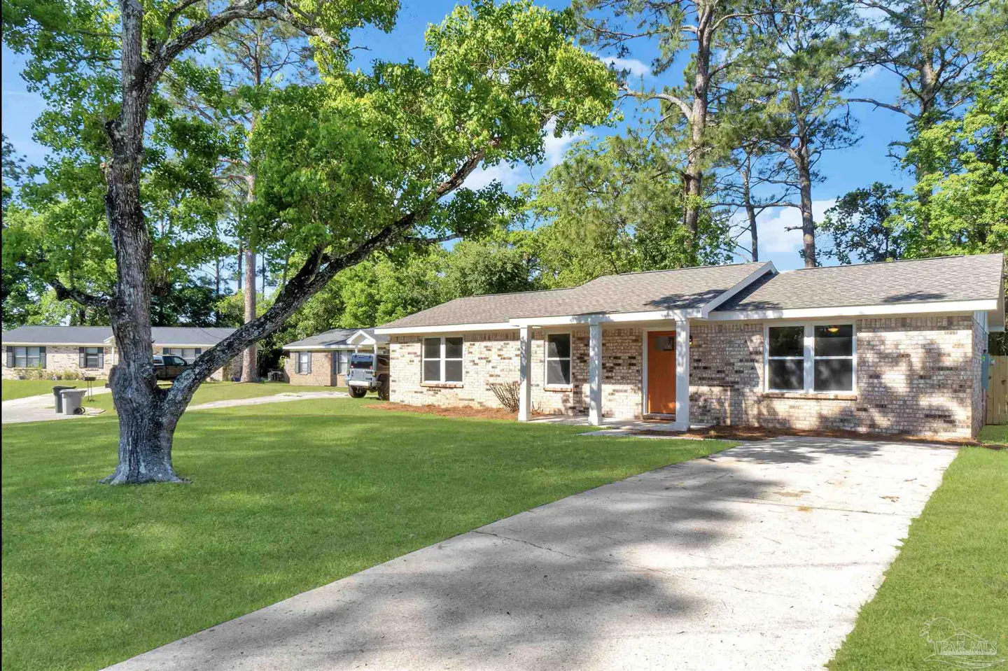 A single-story brick house with an orange door, a concrete driveway, and a green lawn.