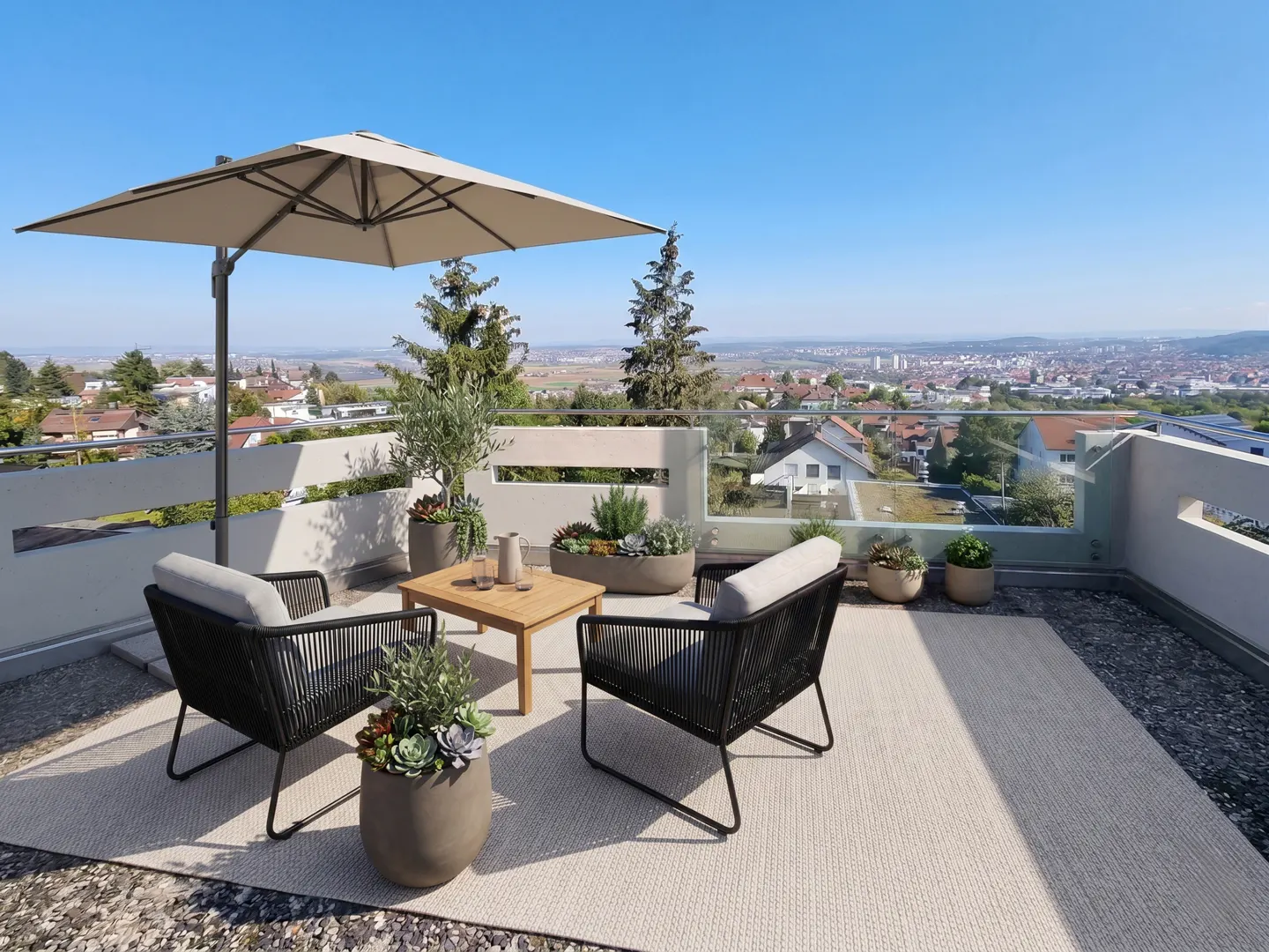 Outdoor patio with two black chairs, a wooden table, and a beige umbrella overlooking a city on a sunny day.