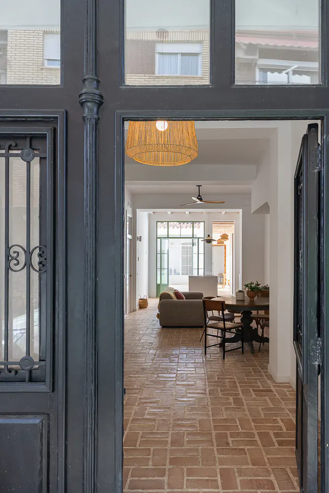 View through an open black door into a home with brick floors, a tan sofa, and a dining table.