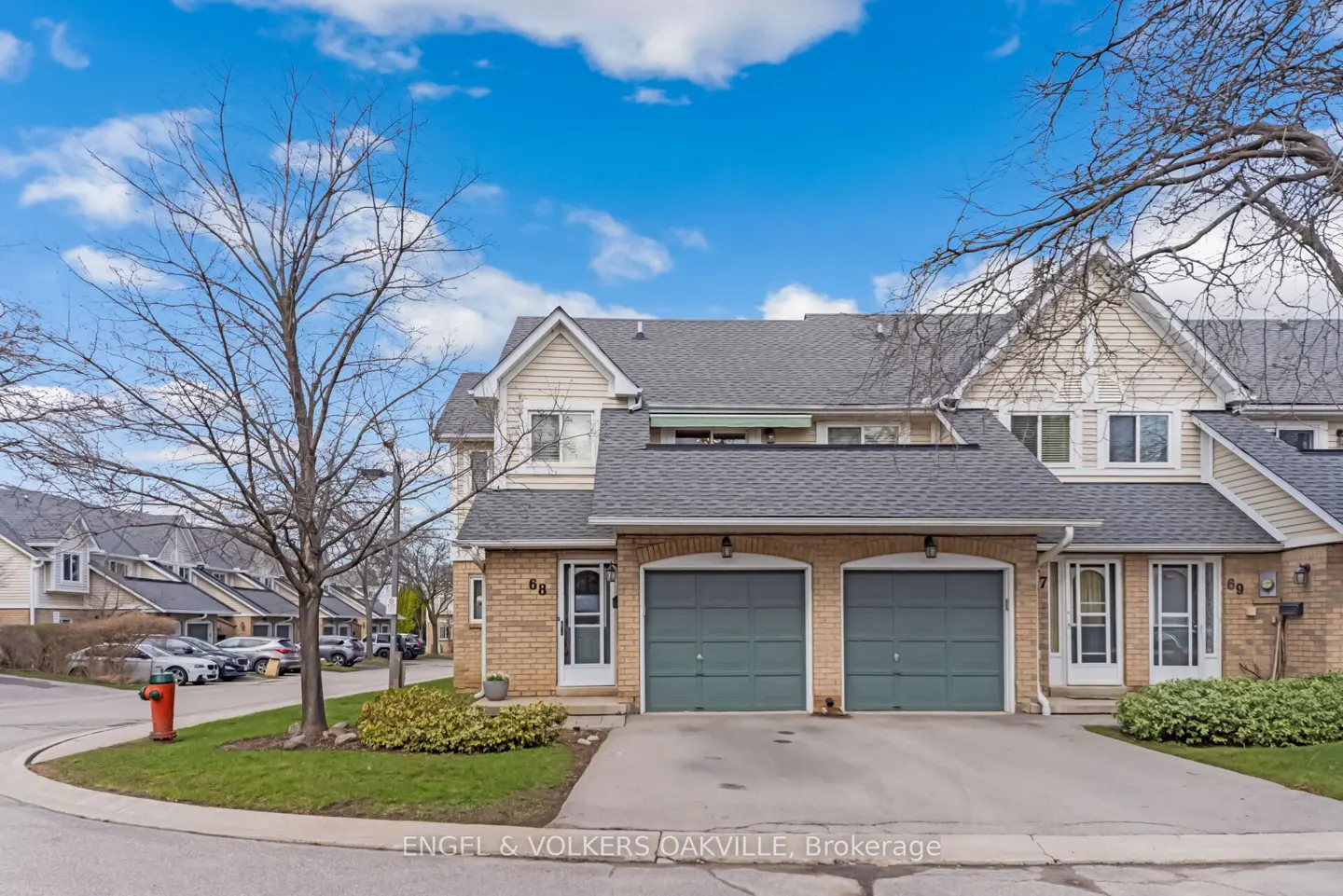 Exterior view of townhouses with brick and siding, green garage doors, and a blue sky.