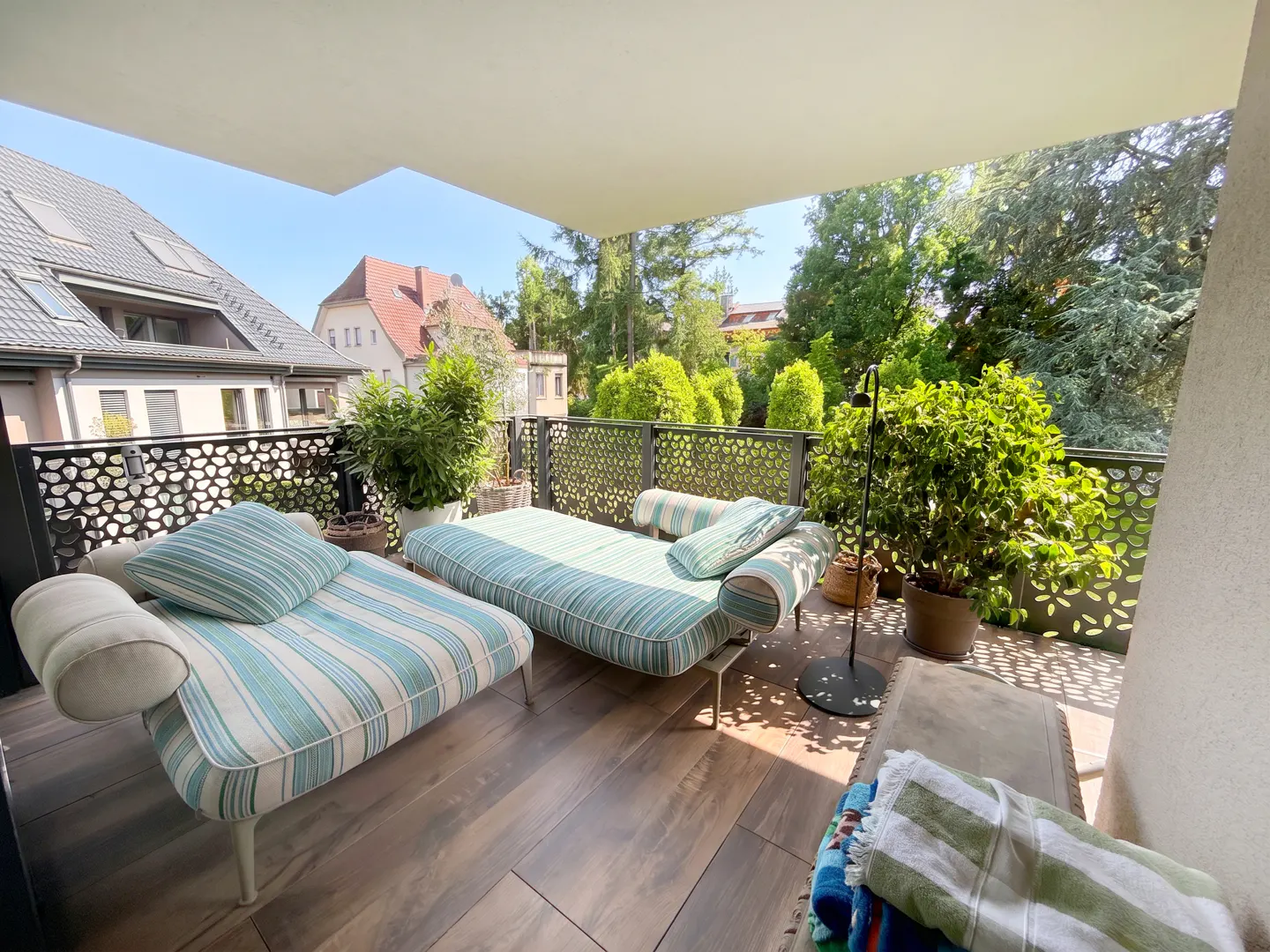 Covered balcony with two striped lounge chairs, potted plants, and a view of neighboring houses and trees.