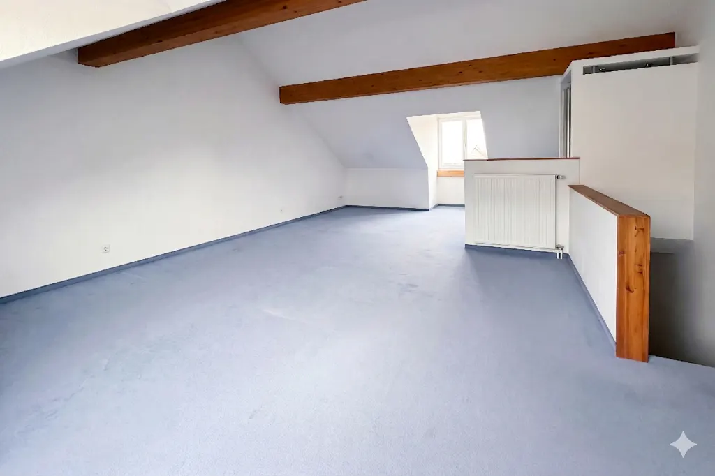 Attic room with blue floor, white walls, and exposed wooden beams. A window and radiator are visible.