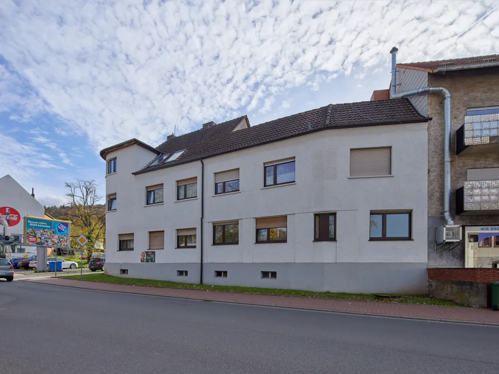 Exterior view of a three-story white building with brown trim and a brown roof. A street runs in front of the building.
