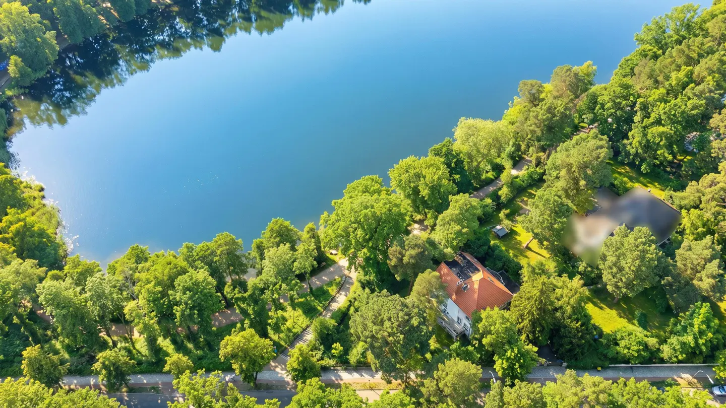 Aerial view of a blue lake surrounded by green trees and a house with a red roof.