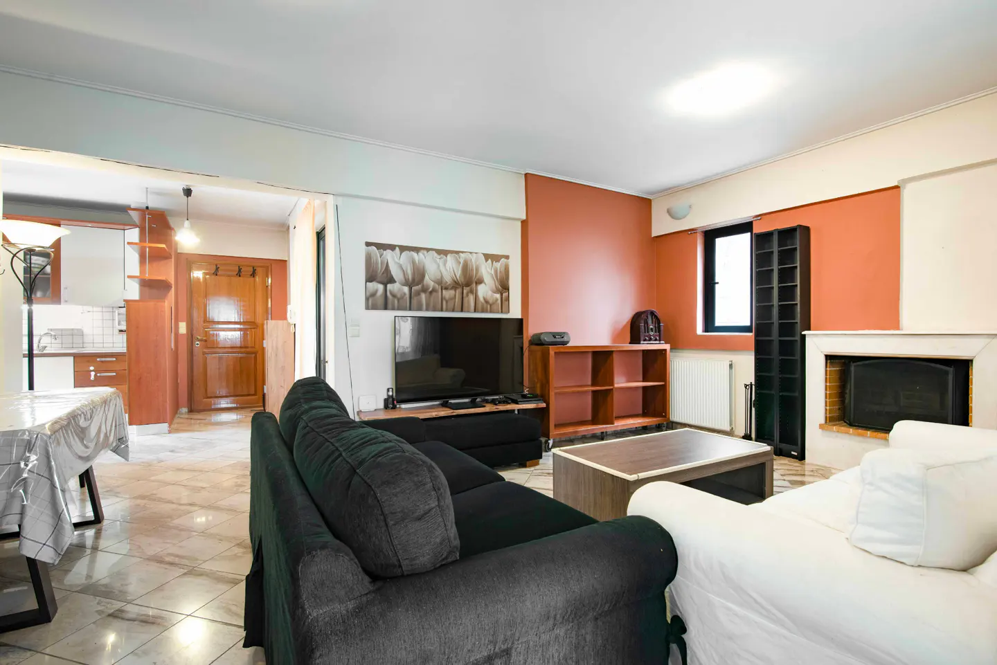 A living room with a black sofa, a white sofa, a TV, and a fireplace. The walls are painted in orange and white.
