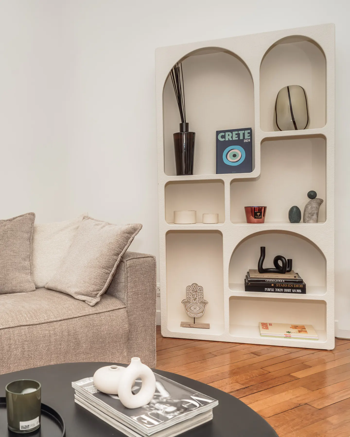 Living room with a beige sofa, black coffee table, and a white arched bookshelf filled with decorative items.