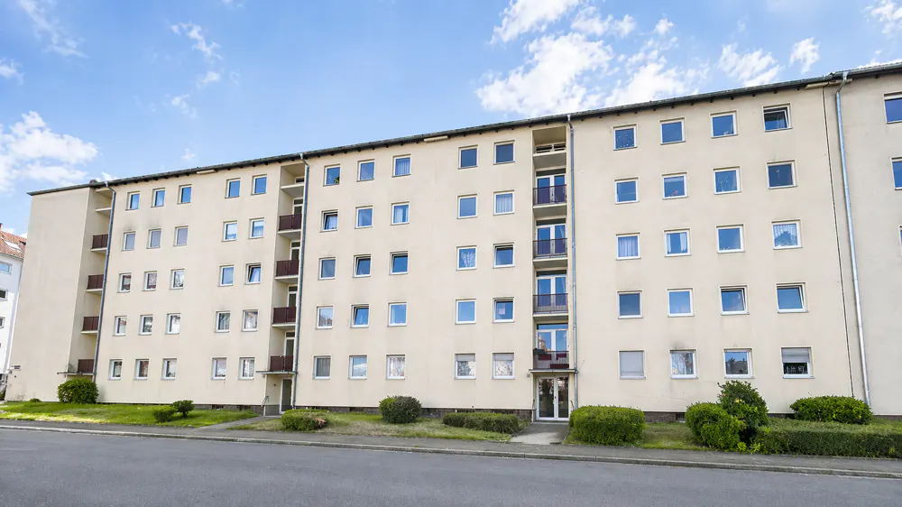 A beige apartment building with many windows and small balconies under a blue sky.