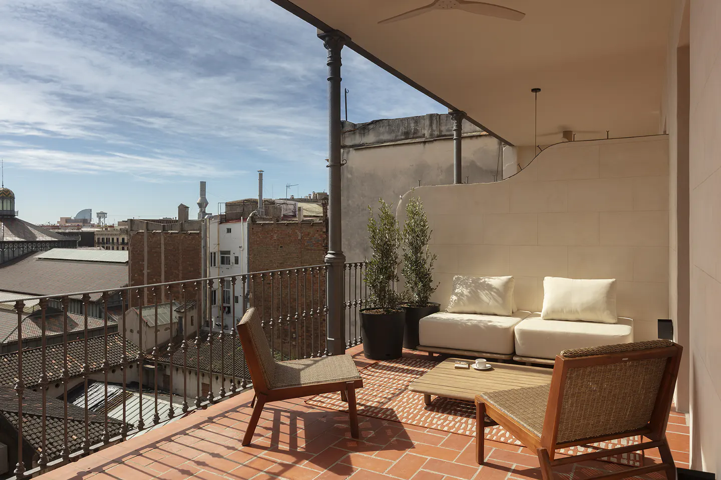 Balcony with terracotta tiles, wrought iron railing, and city view. Outdoor seating includes chairs, a sofa, and a coffee table.