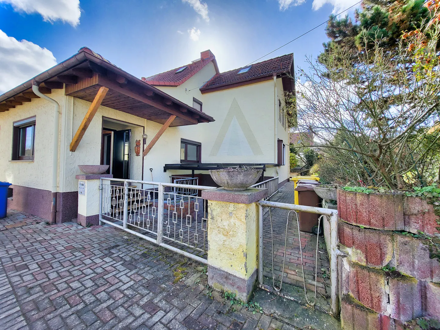 Exterior view of a two-story house with a white fence and brick walkway. The house has a brown roof and a covered porch.