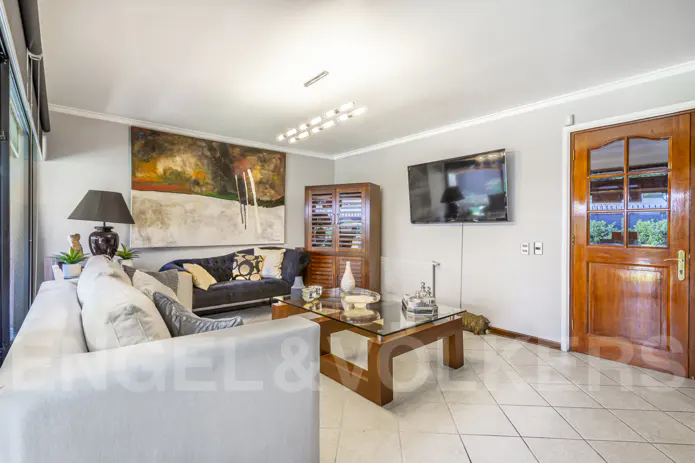 Living room with white sofa, glass coffee table, and dark blue couch. A large abstract painting hangs above the couch. A TV is mounted on the wall.