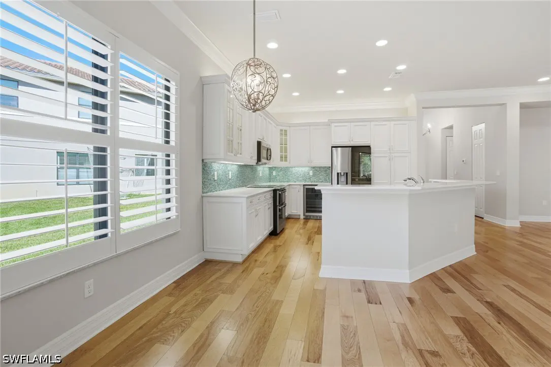 Bright, modern kitchen with white cabinets, stainless steel appliances, and wood floors. A decorative light fixture hangs above the island.