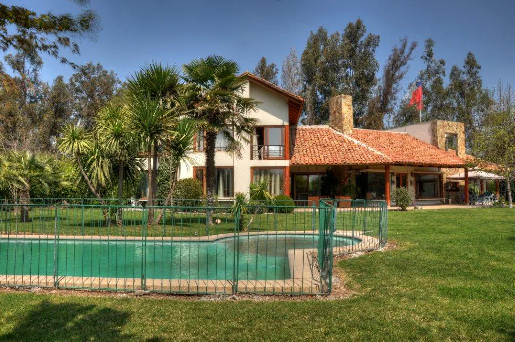 A two-story house with a red tile roof, a pool, and a green lawn on a sunny day.