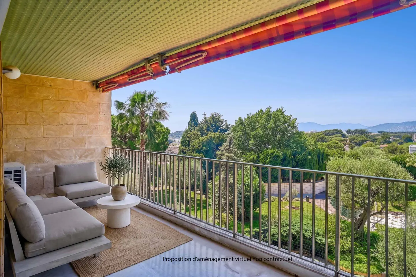 Balcony with stone wall, metal railing, and outdoor furniture overlooking lush greenery and a clear blue sky.