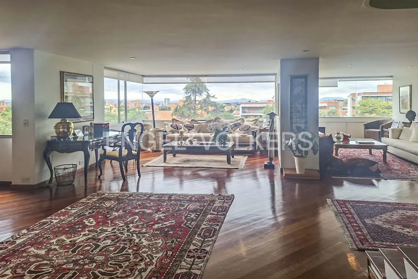 Open-concept living room with hardwood floors, area rugs, and floor-to-ceiling windows with city views.
