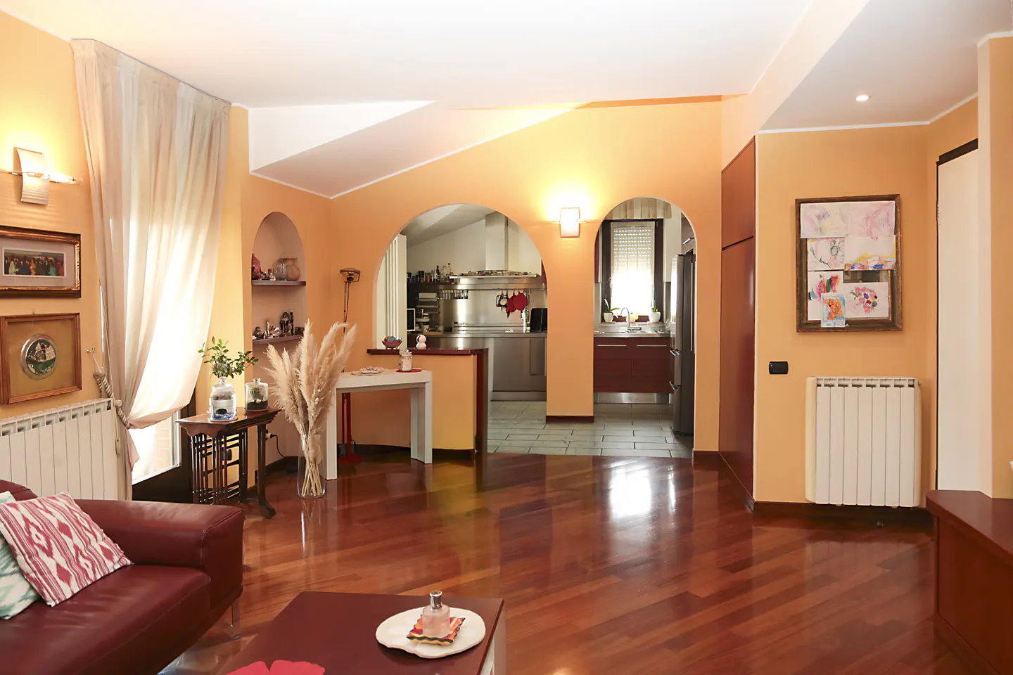Open-concept living room with hardwood floors, peach walls, and arched doorways leading to the kitchen. A red leather sofa is visible.