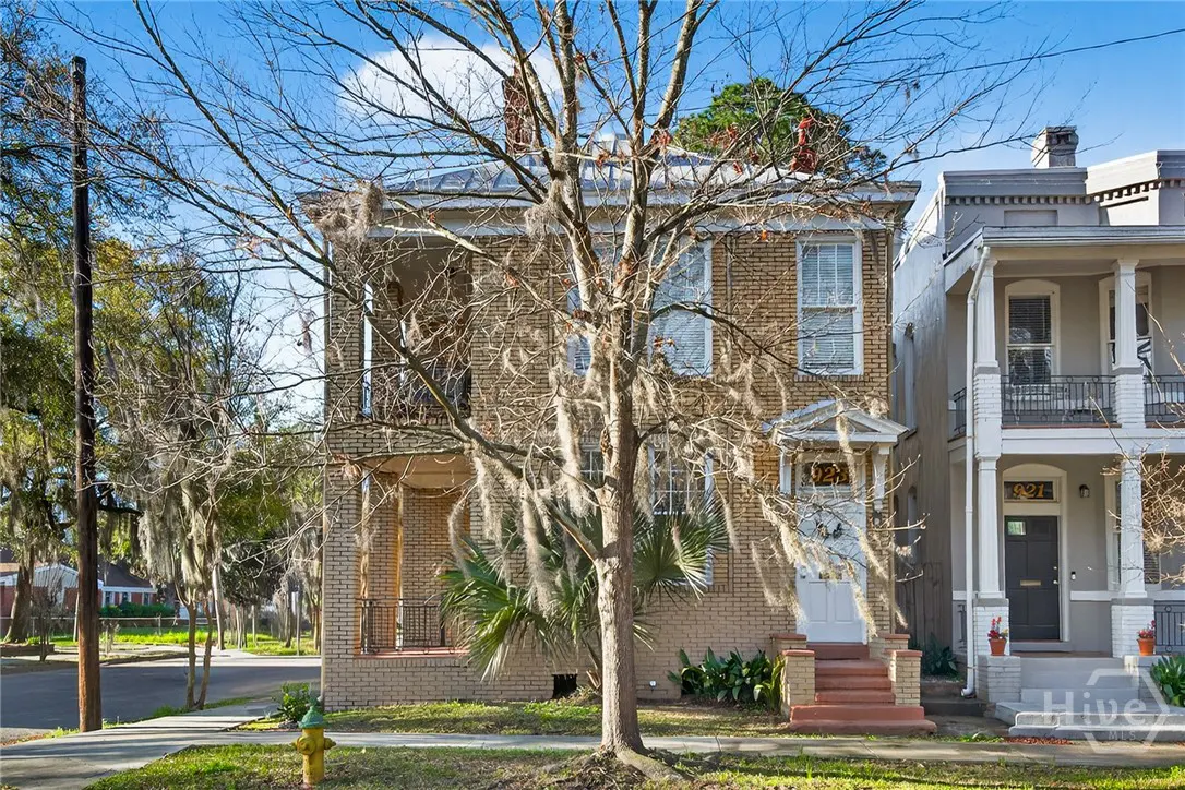 Two-story brick house with a white door and a tree covered in Spanish moss in the front yard.