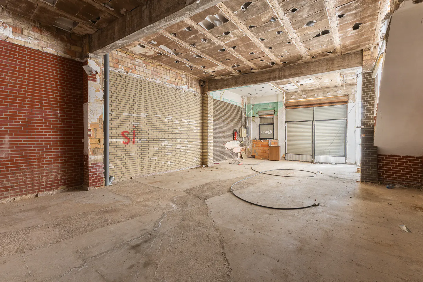 Interior of a commercial space under renovation, featuring exposed brick walls, concrete floors, and a damaged ceiling.