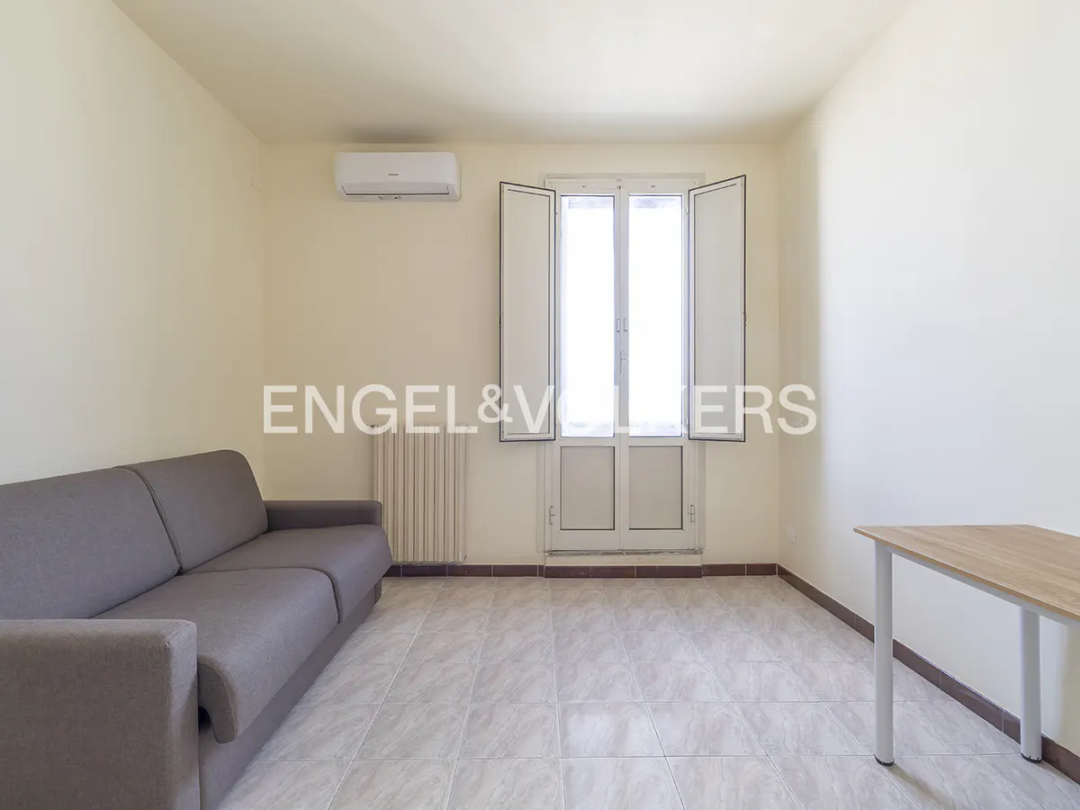 A bright room with a gray sofa, table, and open white shutters on a window.
