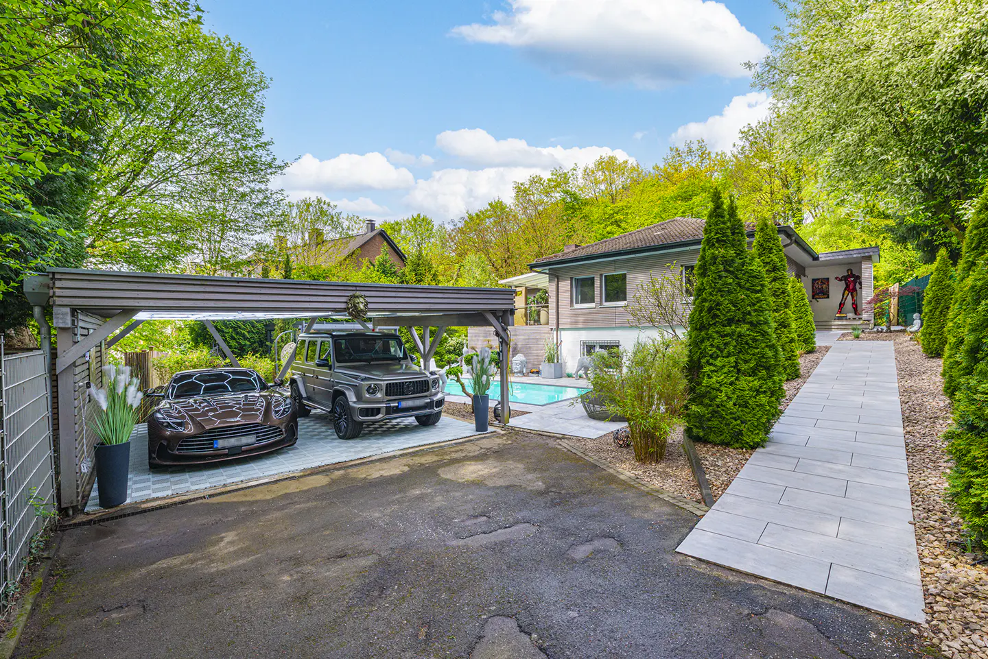 Luxury home exterior with a carport holding a brown sports car and a gray SUV, a pool, and a stone walkway.