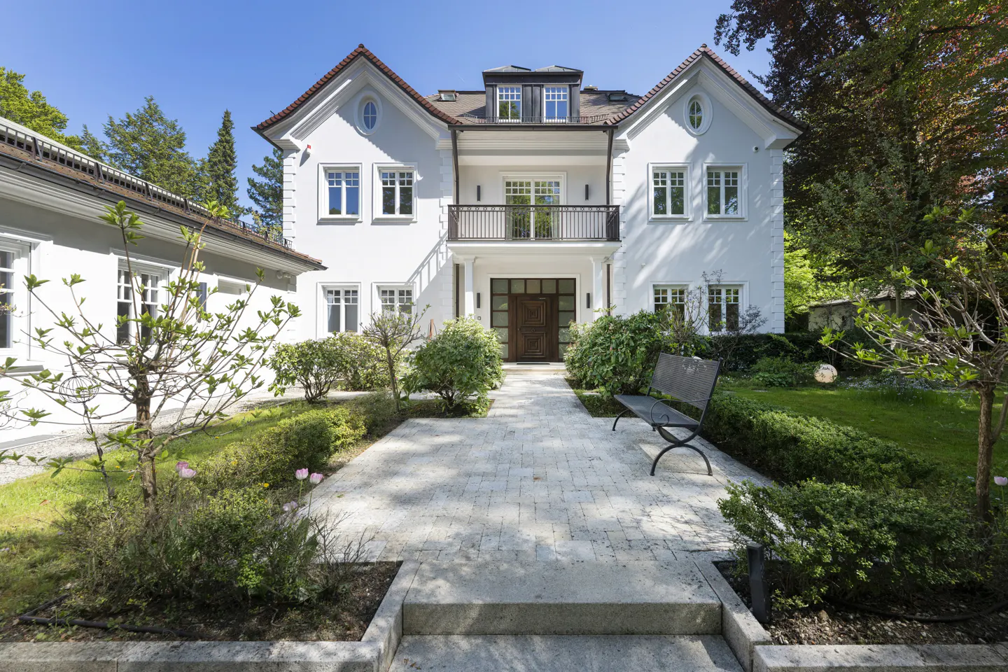 Exterior view of a two-story white house with a red tile roof, a stone walkway, and a black bench.