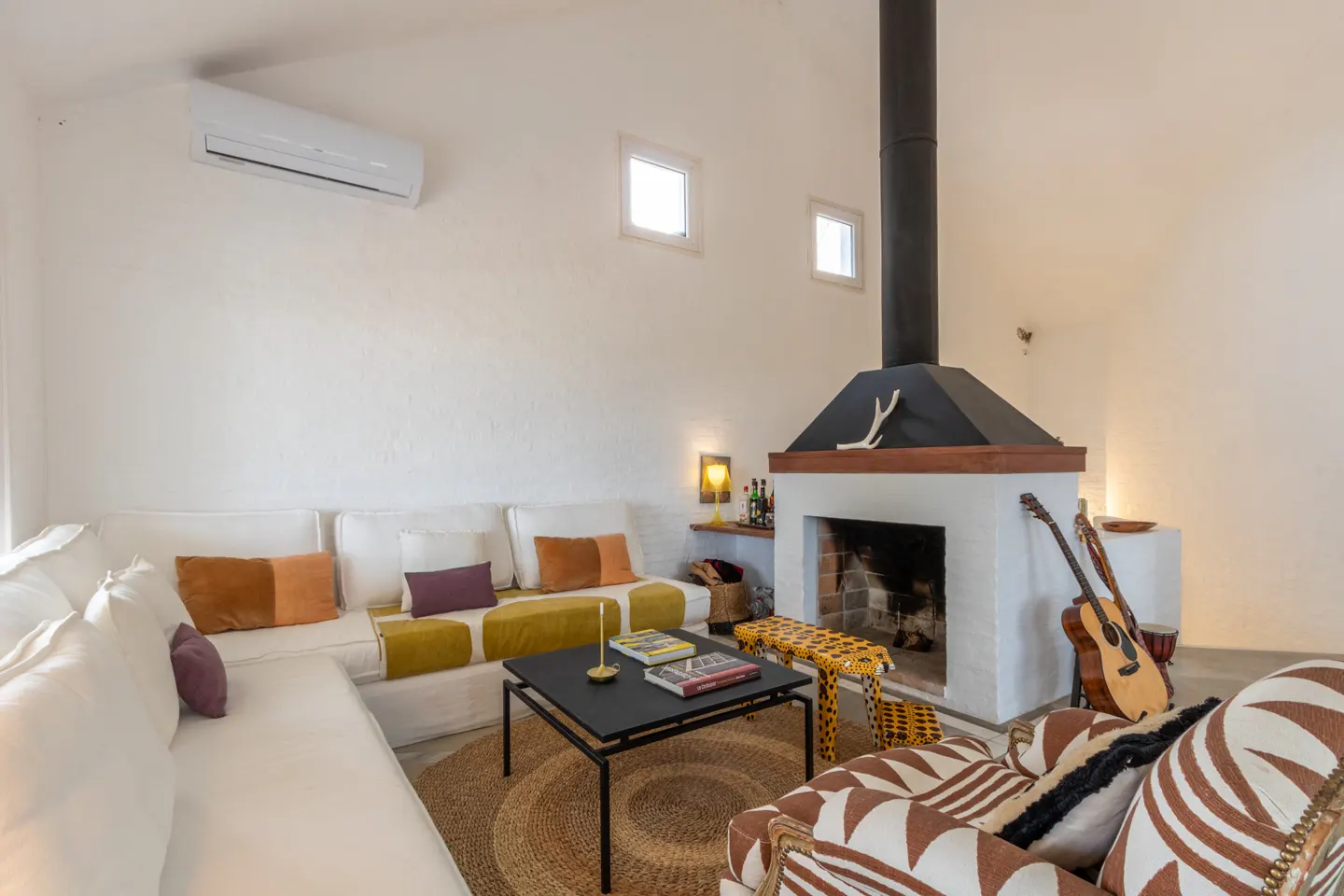 Living room with white walls, a white sectional sofa, a black coffee table, a fireplace, and a patterned armchair.