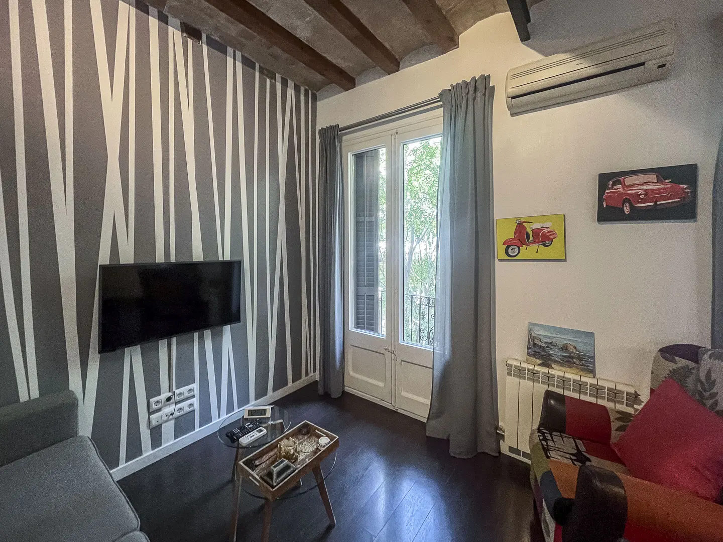 Living room with gray striped wallpaper, wall-mounted TV, glass coffee table, and balcony doors with gray curtains.