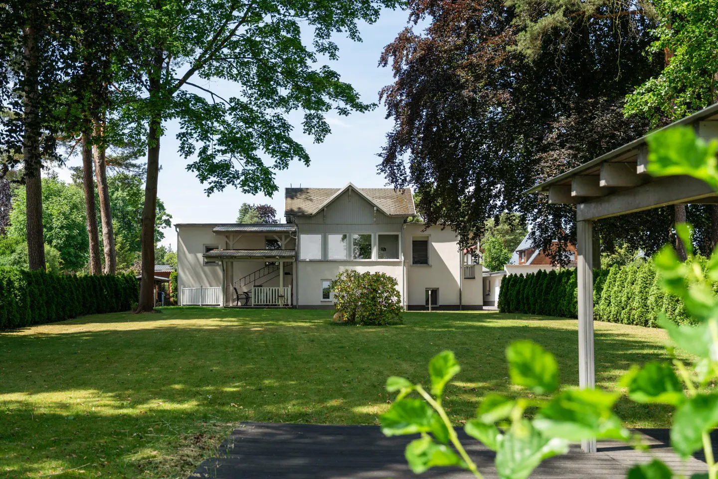 Backyard view of a two-story gray house with a green lawn and trees. A staircase leads to a second-story porch.