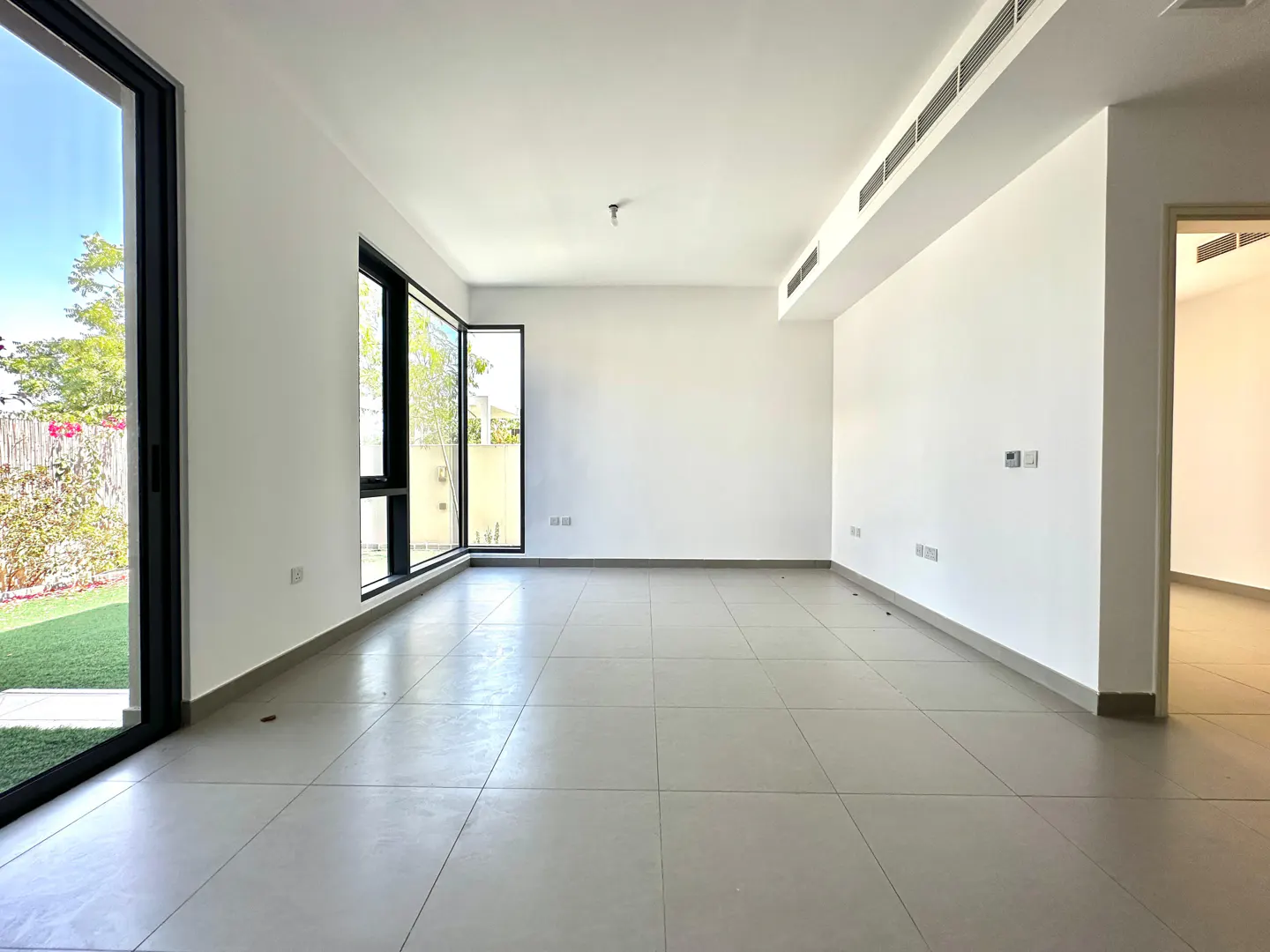 Empty room with white walls, gray tile floor, and black-framed windows overlooking a green lawn.