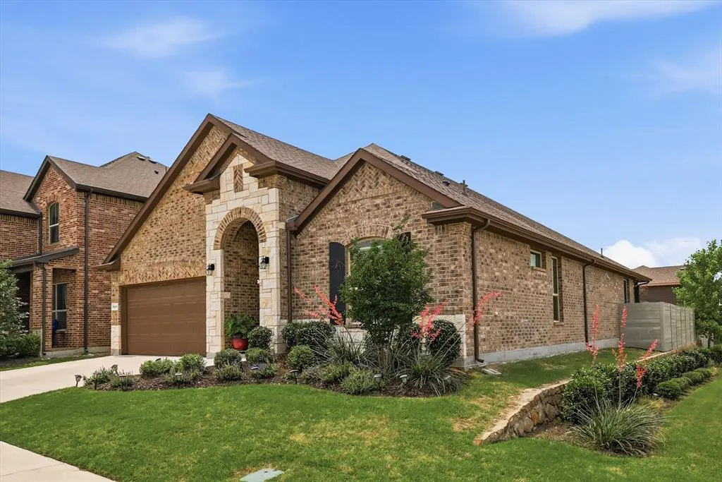 A single-story brick house with a brown roof, a stone archway, and a brown garage door under a blue sky.