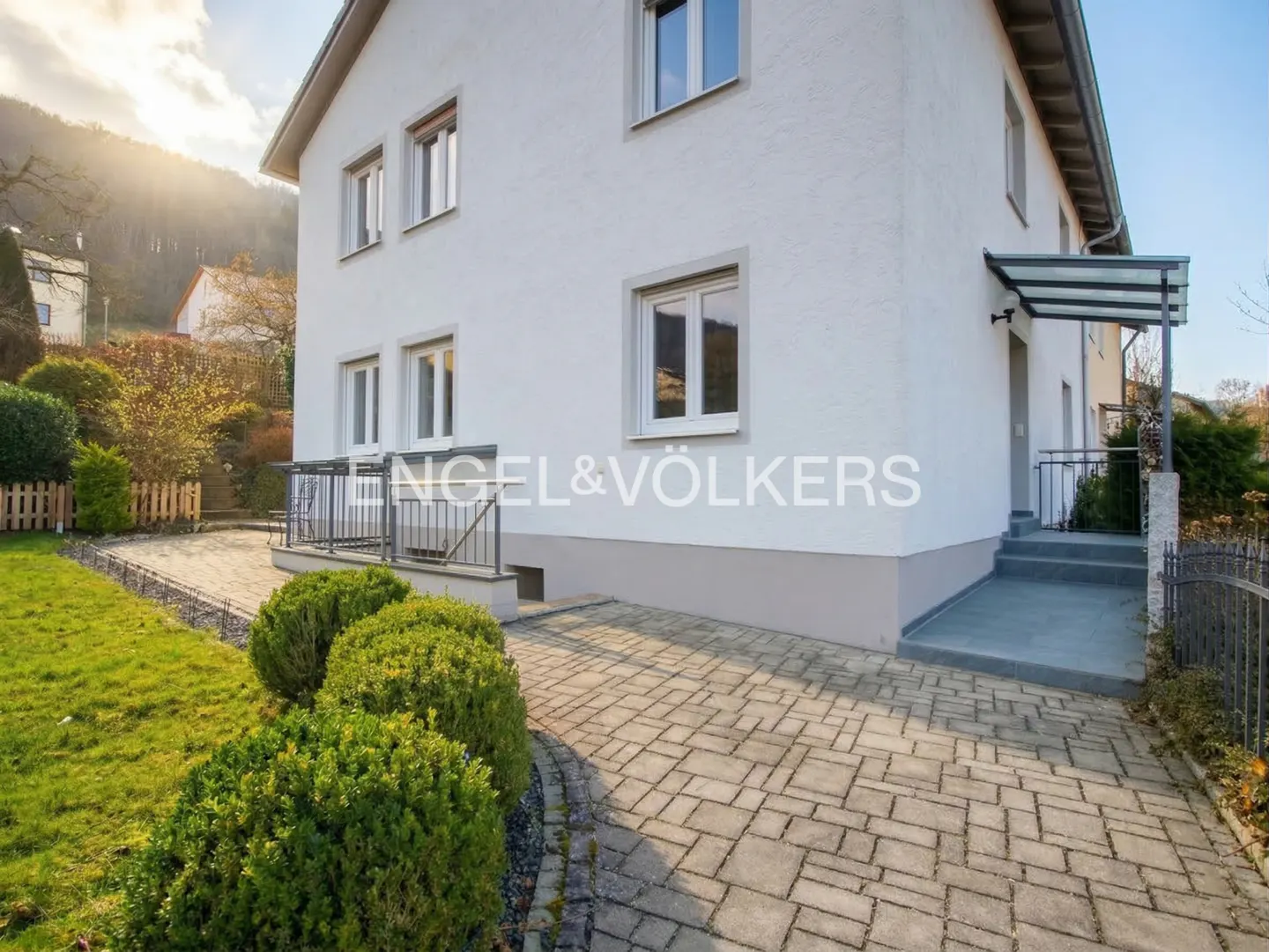 Exterior of a two-story white house with a stone walkway and green bushes. Engel & Völkers logo is visible.