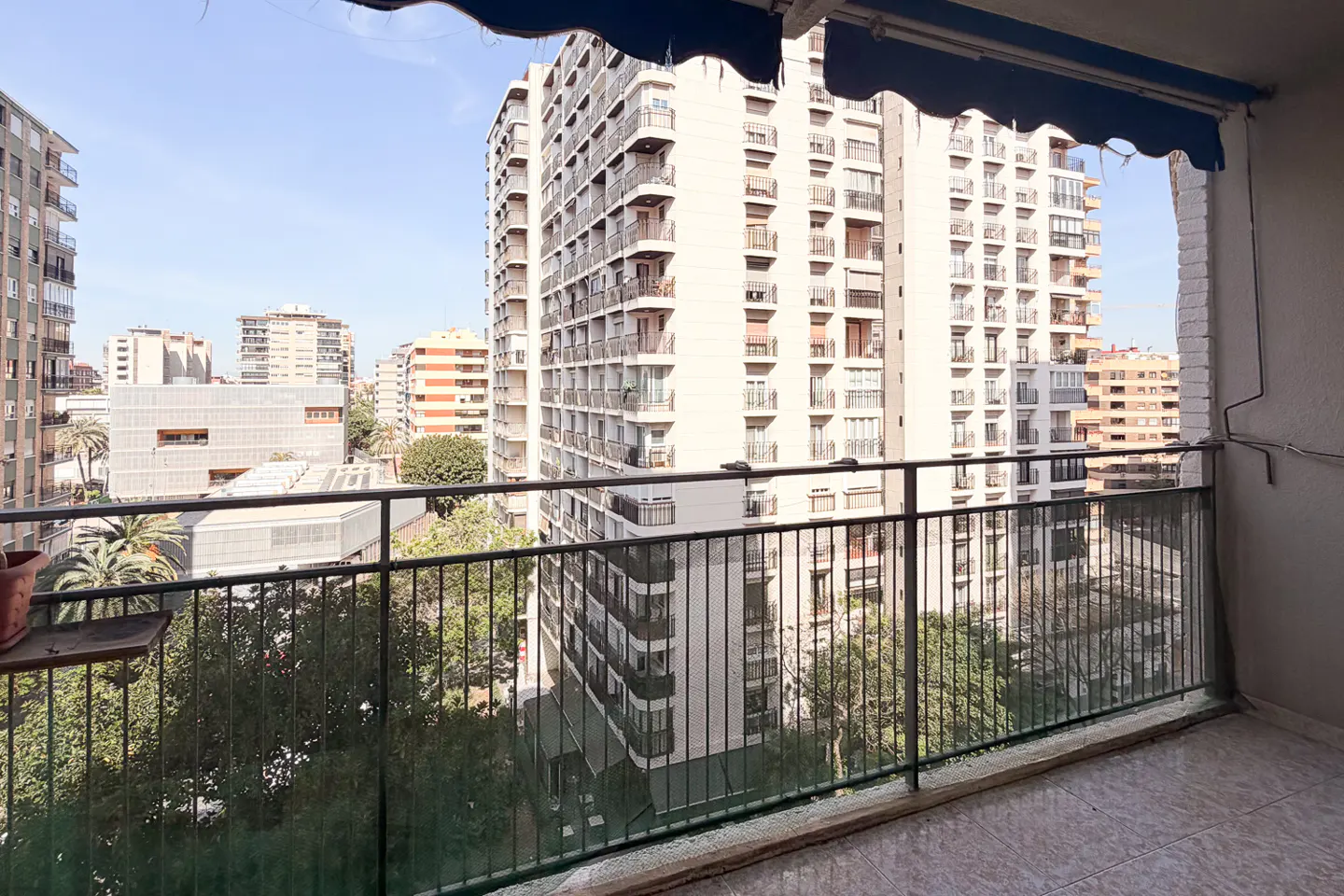 View from a balcony with black railings overlooking city buildings and trees on a sunny day.