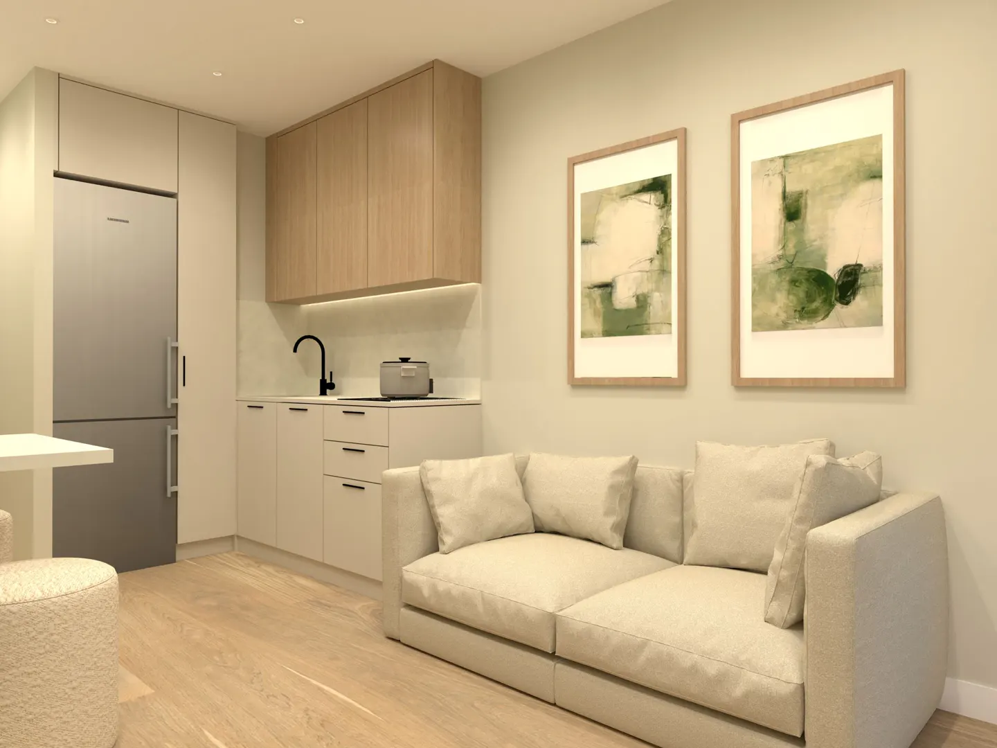 Studio apartment with a beige sofa, framed art, and a kitchen with light wood cabinets and stainless steel appliances.