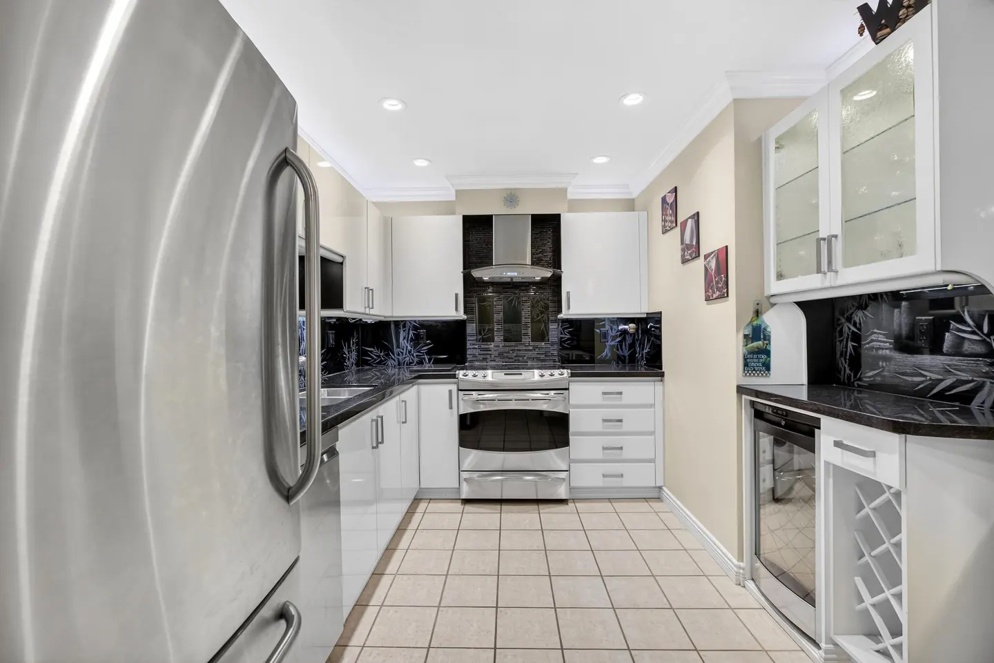 Bright kitchen with stainless steel appliances, white cabinets, black countertops, and beige tile flooring.
