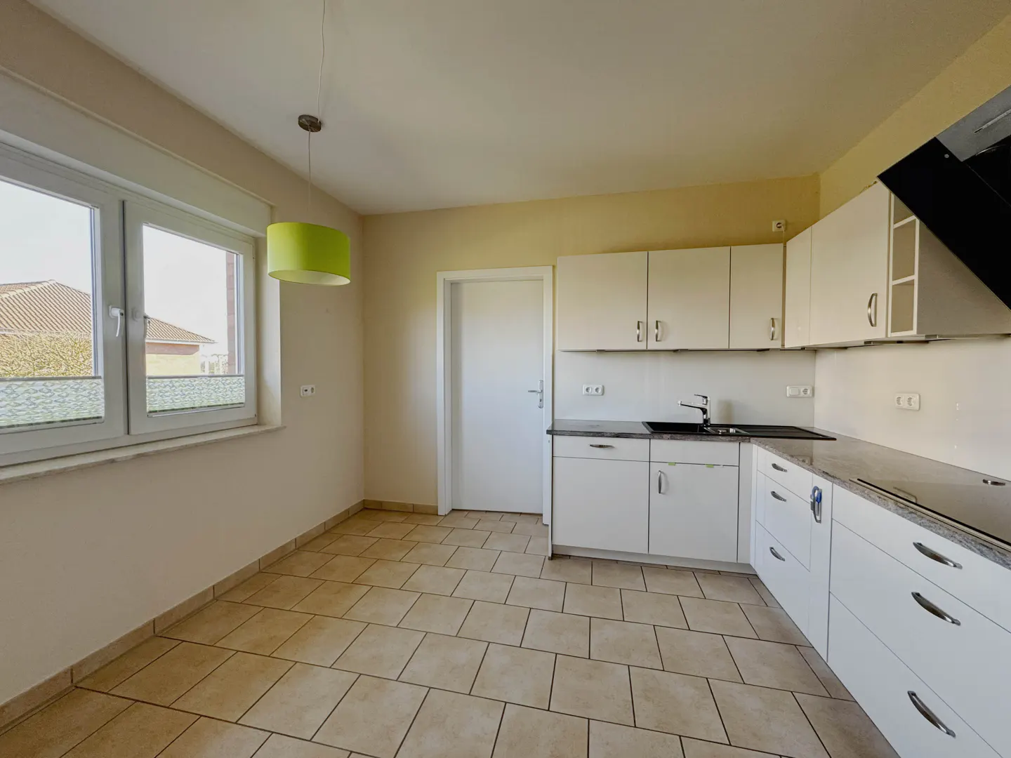 Bright kitchen with white cabinets, black countertops, and beige tile floor. A green pendant light hangs near a window.