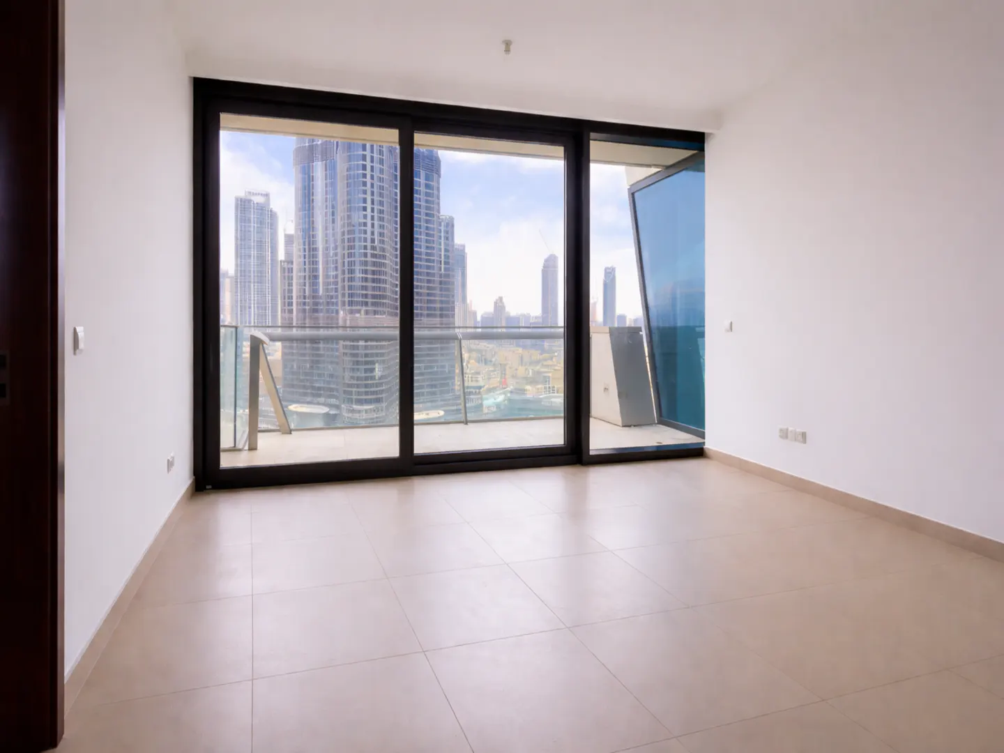 Empty room with white walls, beige tile floors, and large sliding glass doors opening to a balcony with city skyline views.