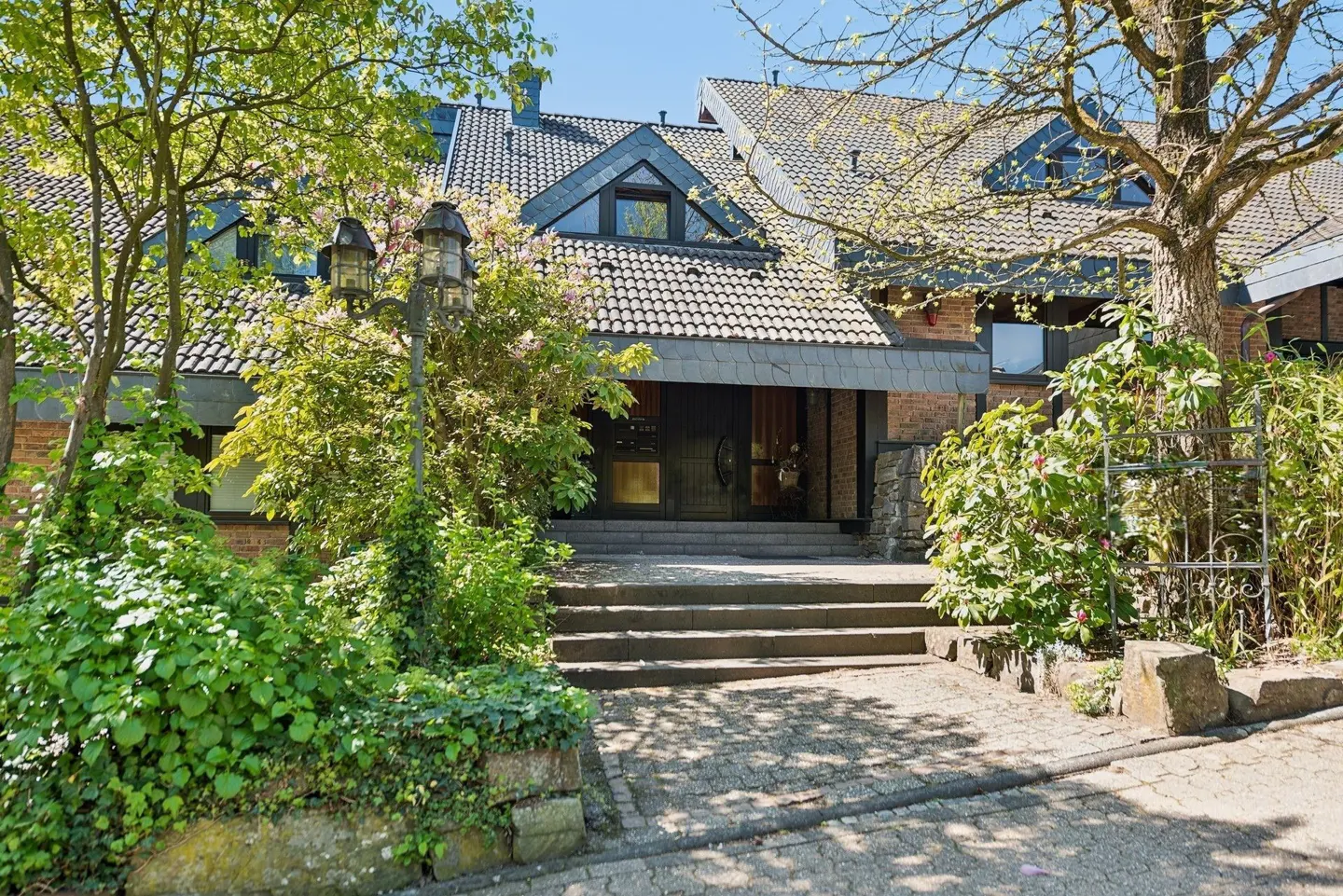 Exterior view of a two-story house with a gray tiled roof, brick walls, and a stone walkway leading to the front door.
